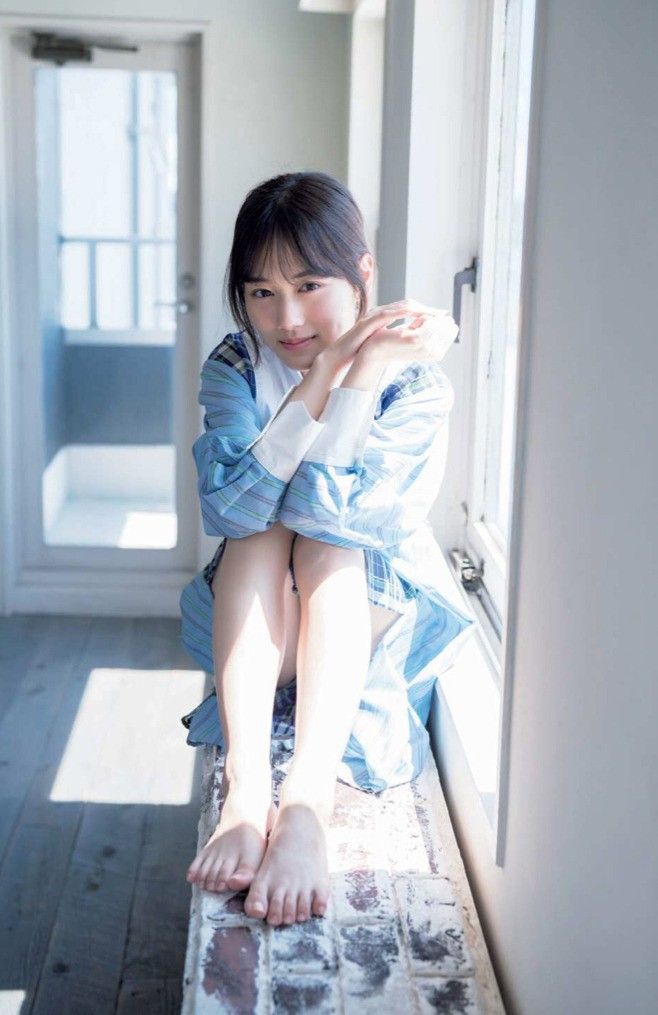Woman in a plaid shirt sitting by a window with bare feet