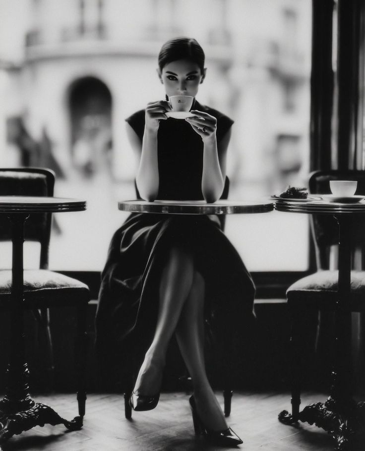 Woman in an elegant dress sitting at a cafe table, holding a coffee cup