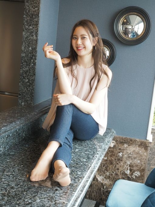 Woman with long hair wearing jeans and a sleeveless top, sitting indoors