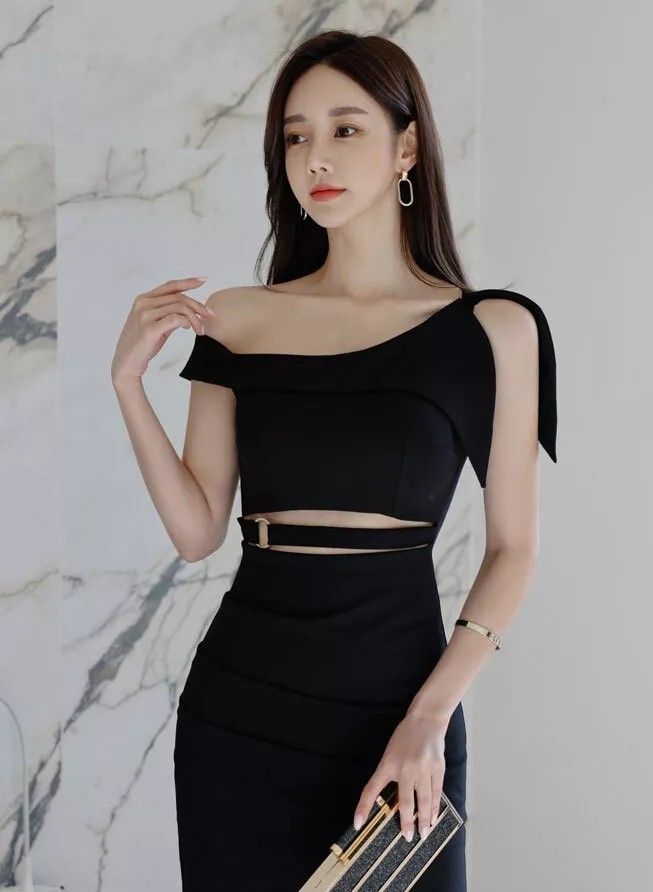 Woman in a black off-shoulder cutout dress holding a clutch bag
