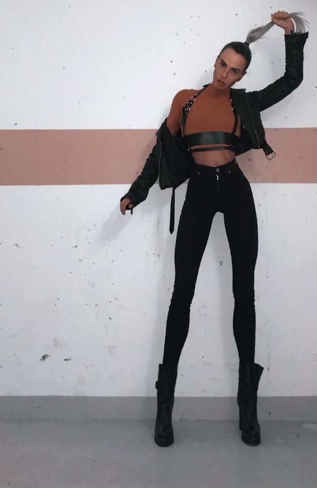 Person in a black leather jacket and jeans with a harness posing indoors