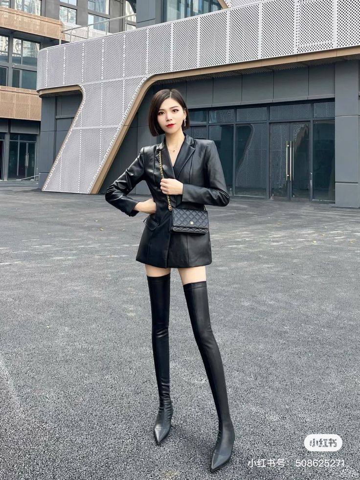 Woman in a black leather blazer and thigh-high boots posing outdoors