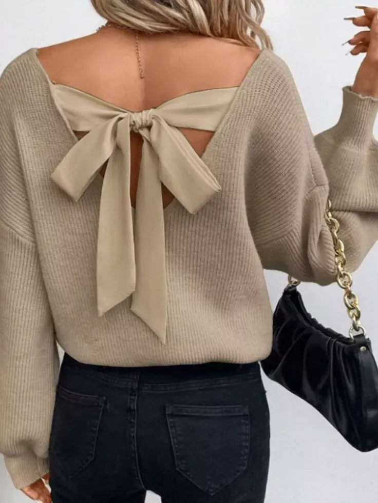 Woman in a beige knitted sweater with a bow detail on the back and black jeans