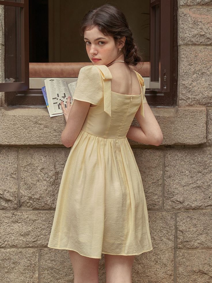 Woman in a yellow dress with braided hair holding a book, looking back over her shoulder