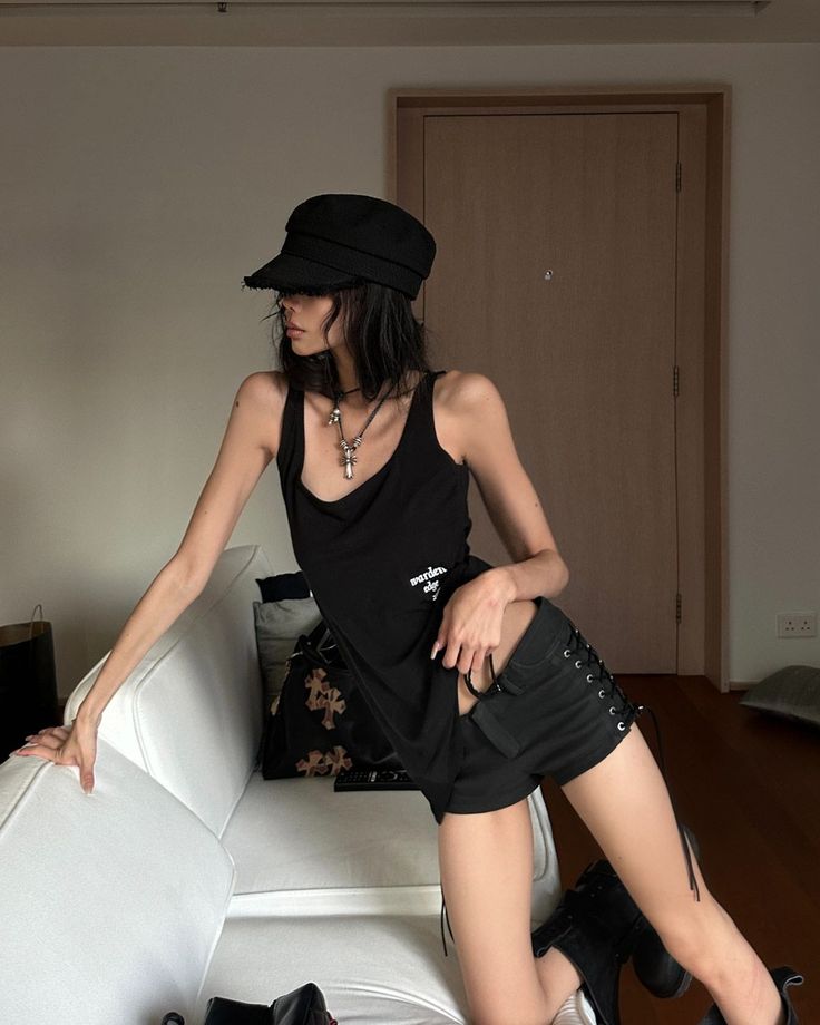 Woman in a black tank top and shorts with a hat, kneeling on a couch