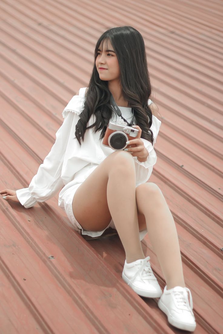 Young woman with long dark hair sitting outdoors, holding a camera