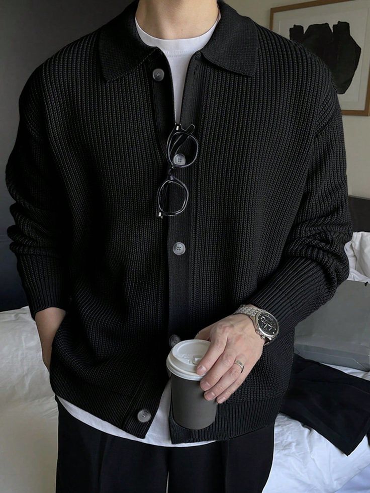 Person wearing a black cardigan over a white t-shirt, holding a coffee cup