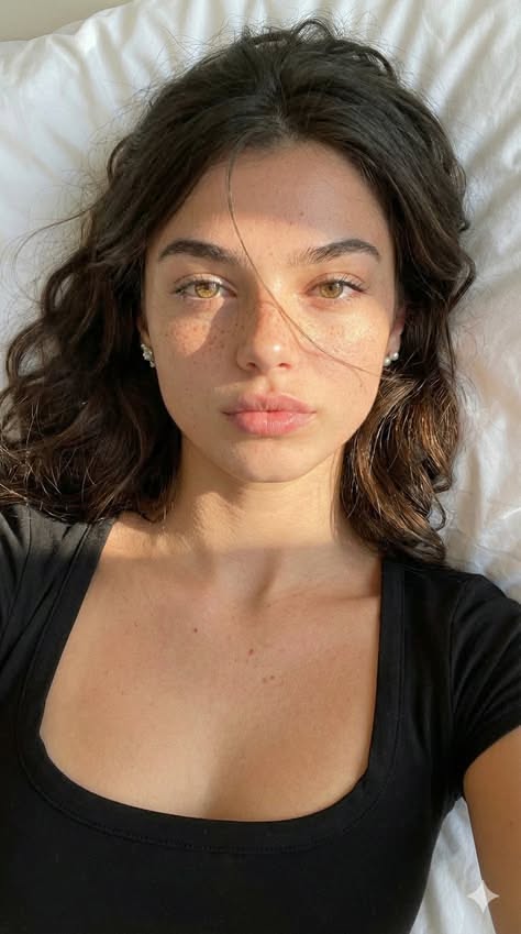 Woman with freckles and long brown hair wearing a black top, lit by soft sunlight