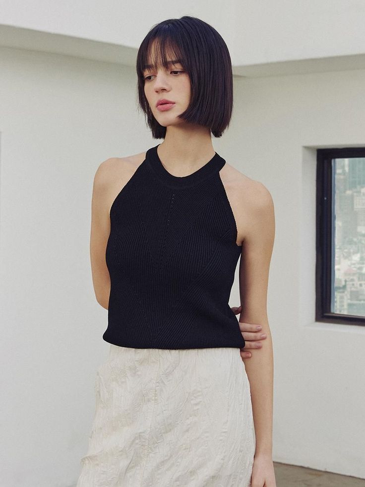 Woman with short black hair wearing a black top and white skirt indoors
