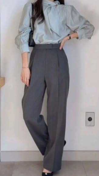 Person in a light blue blouse and dark gray wide-leg pants with a black handbag