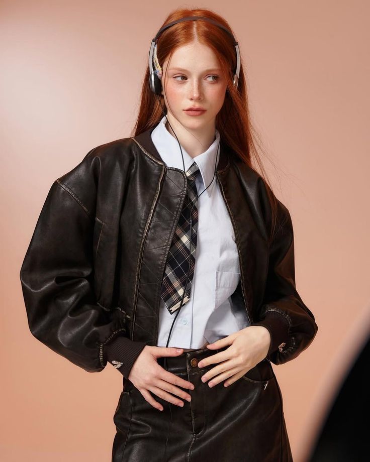 Woman with red hair wearing headphones, a leather jacket, and a plaid tie
