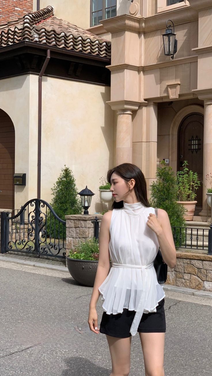 Woman in a white top and black shorts standing outdoors in daylight