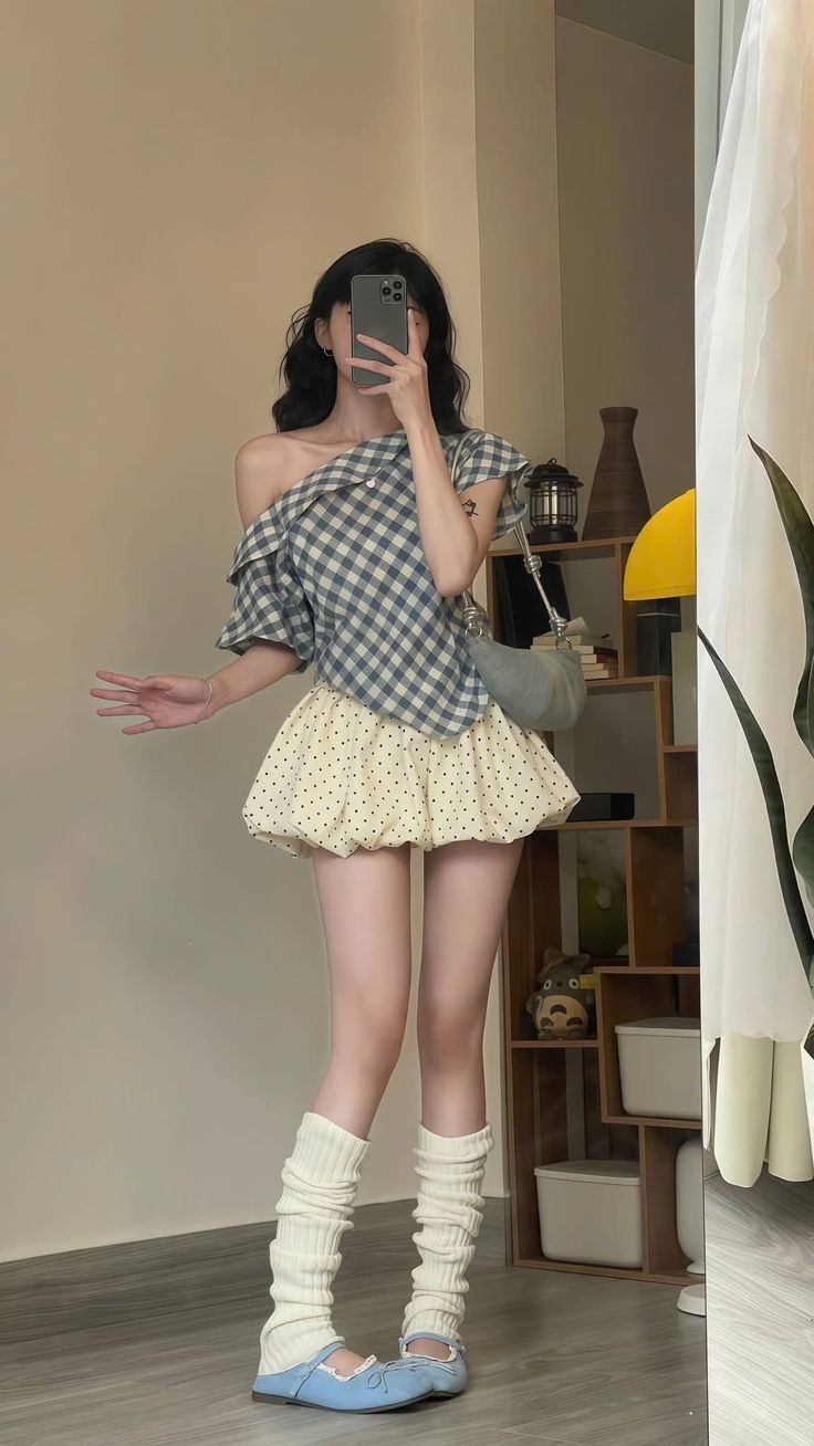 Woman in a plaid top and polka dot skirt taking a mirror selfie