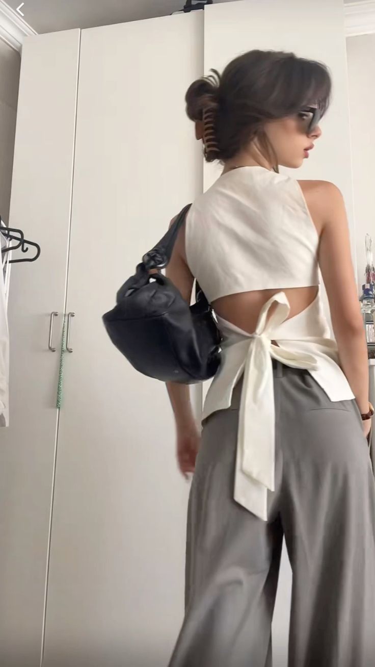 Woman in a white open-back top with a bow tie and gray pants indoors