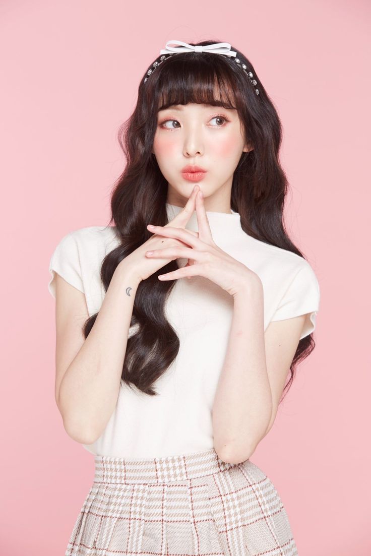 Woman with long dark hair and a plaid skirt against a pink background