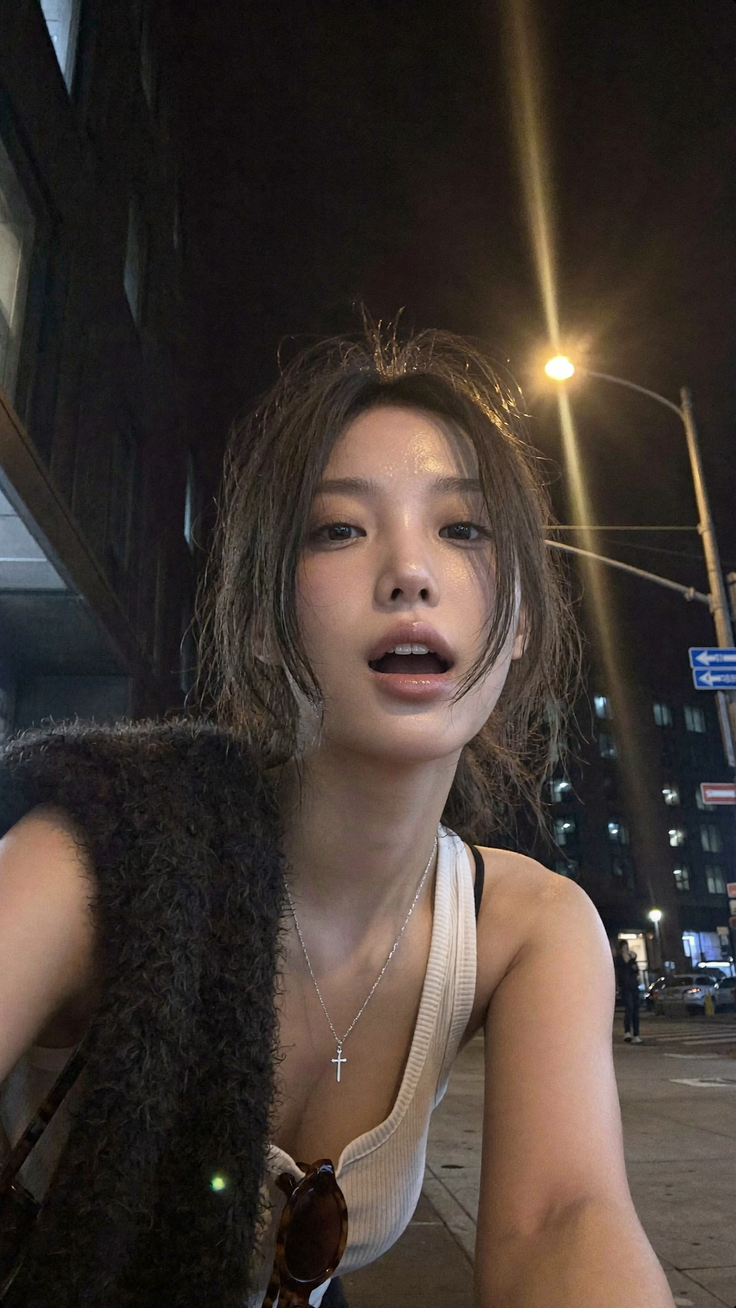 Woman in a white tank top and cross necklace on a street at night