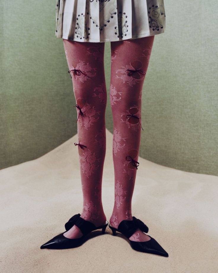 Lower body of a person wearing pink lace tights with bows and black kitten heels