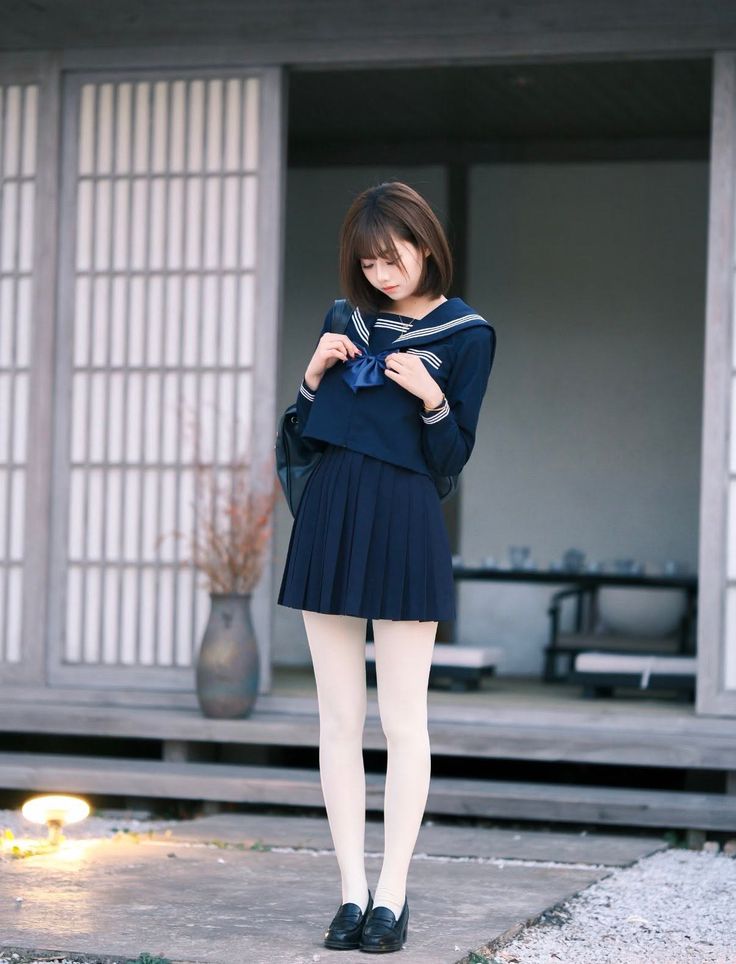 Woman in a school uniform with a pleated skirt and white tights outdoors
