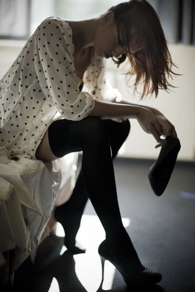 Woman in a polka dot shirt and thigh-high stockings holding a high heel