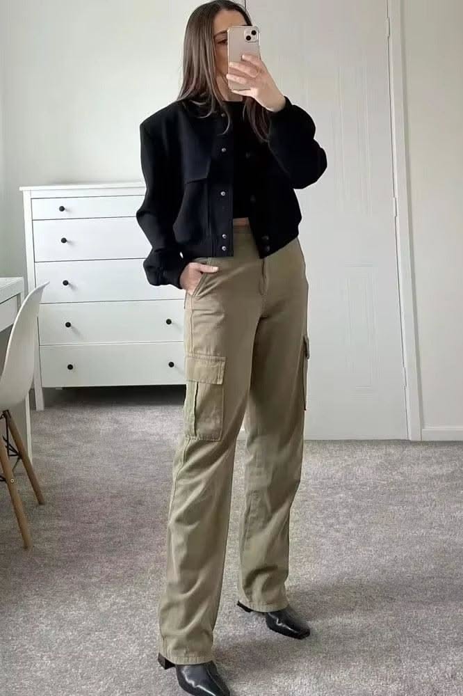 Woman in a black jacket and cargo pants taking a mirror selfie indoors