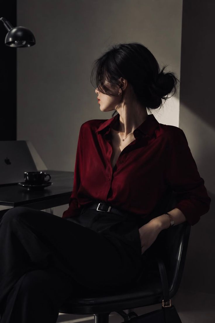Woman in a red shirt and black pants sitting indoors with dramatic lighting