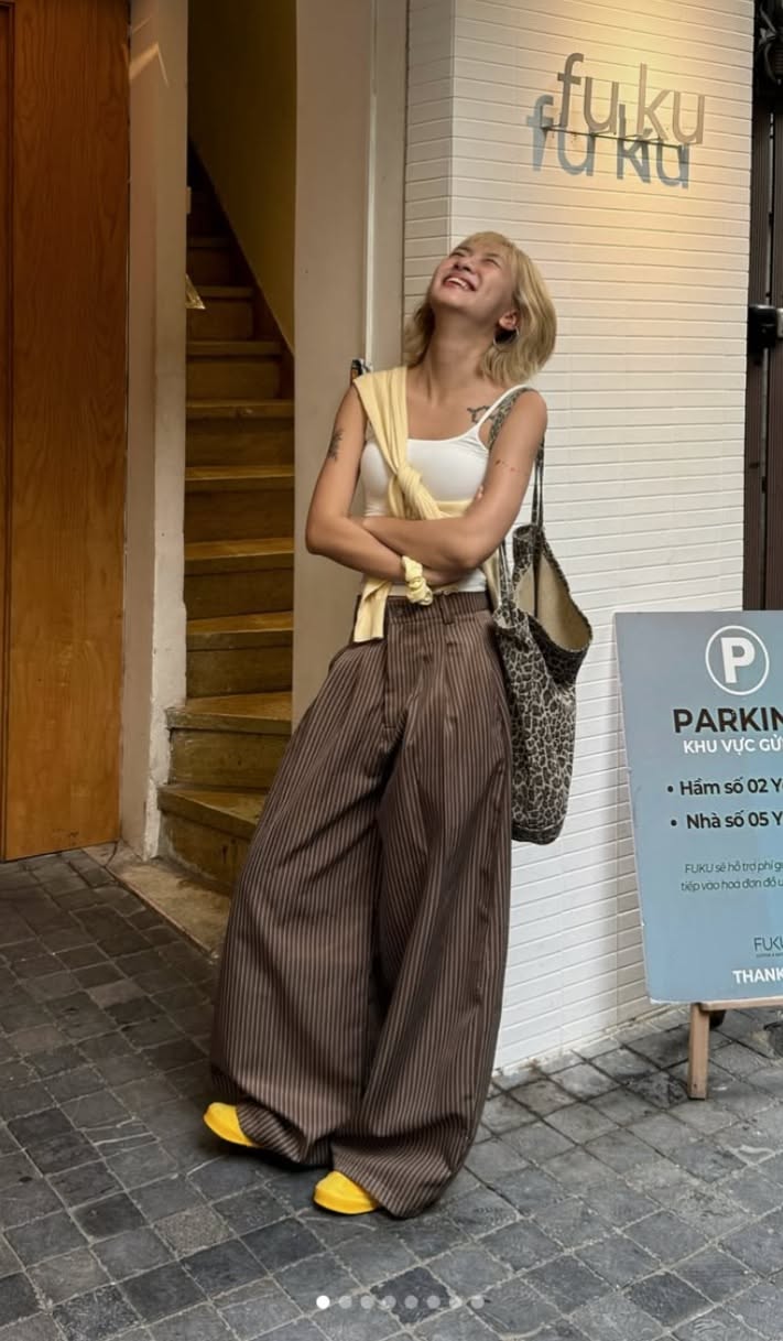 Woman with blonde hair wearing wide leg pants and a white tank top outdoors