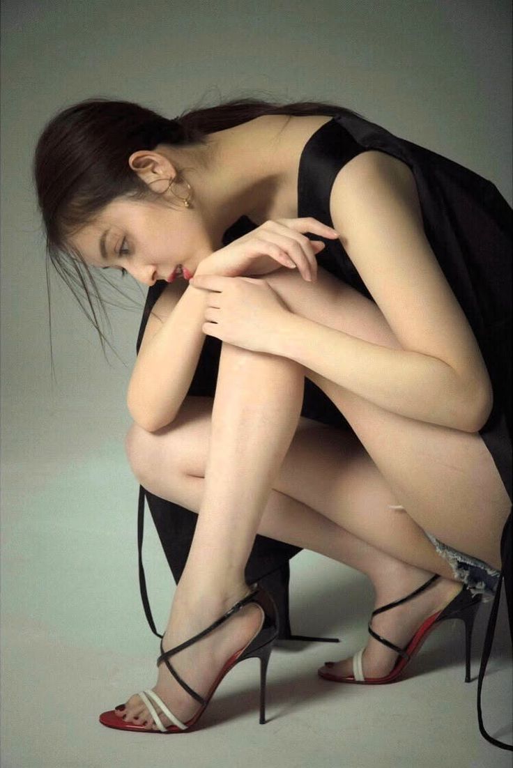 Woman in a black dress and high heels squatting in a studio