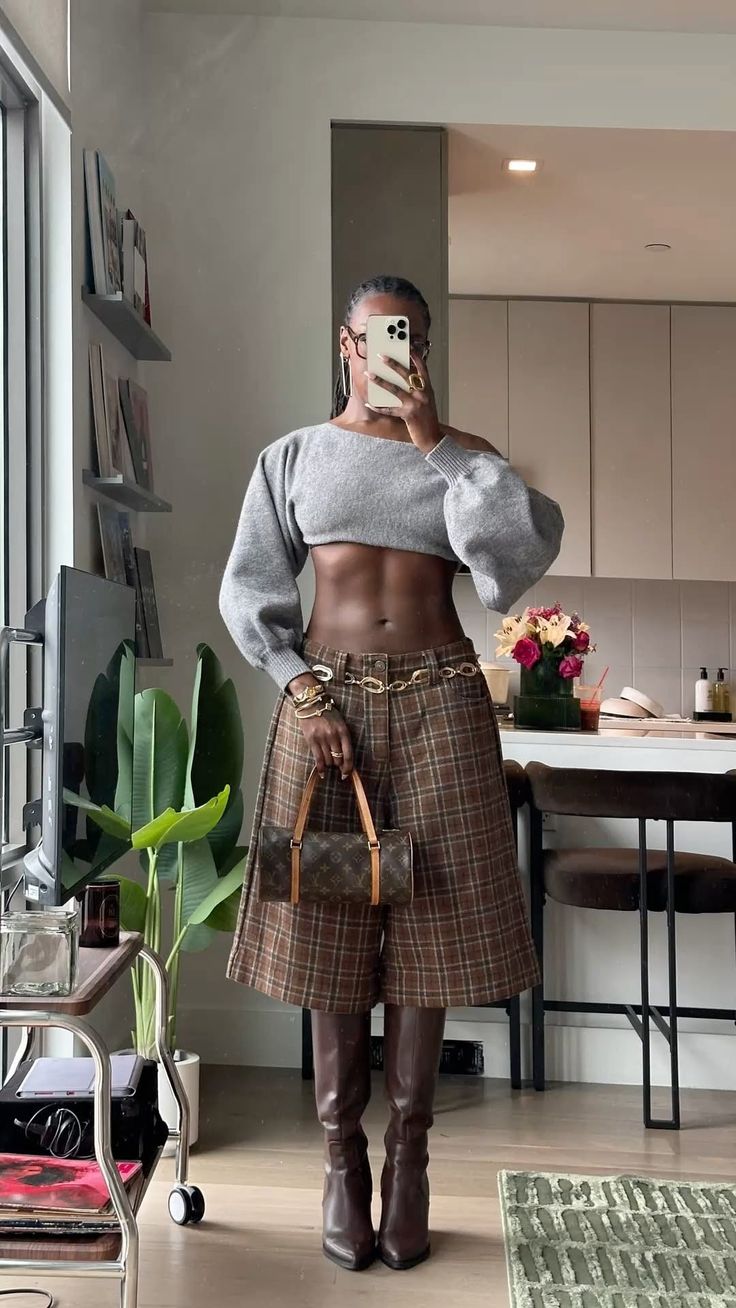 Woman in a gray crop top and plaid skirt taking a mirror selfie