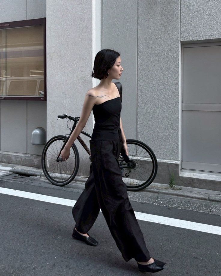 Woman with short black hair walking on a street next to a bicycle