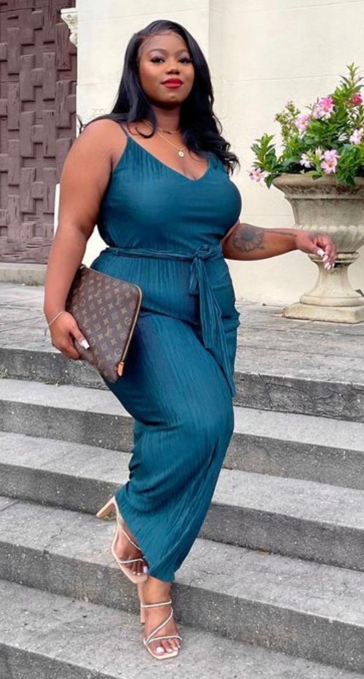 Woman in a teal jumpsuit and heeled sandals standing on outdoor stairs