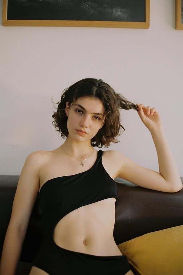 Woman in a black one-shoulder swimsuit with a cutout, pulling her hair