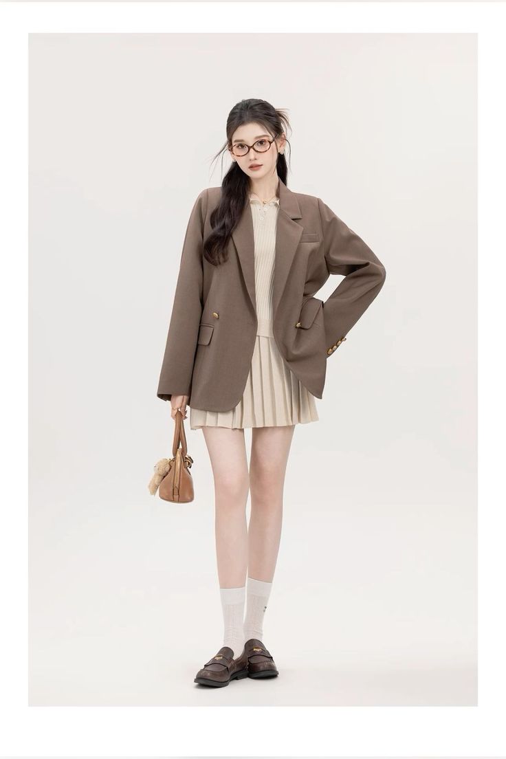 Woman in a brown blazer and pleated skirt holding a small bag