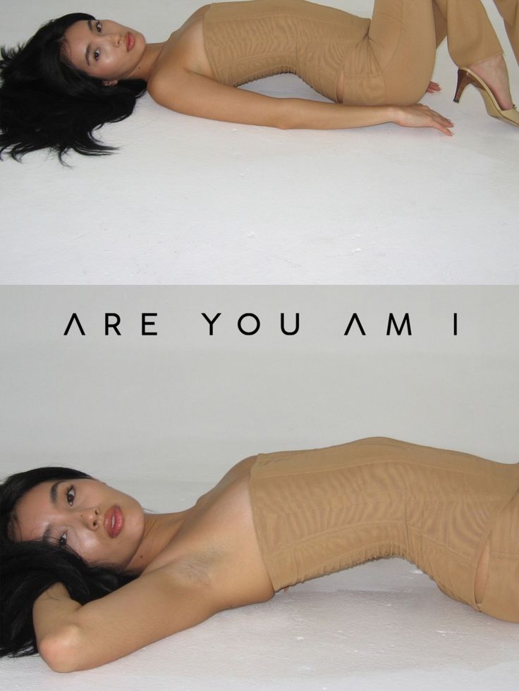 Woman with long black hair wearing a strapless top and tan pants, lying on a white surface