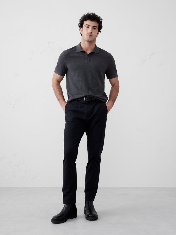 Man in a dark grey polo shirt and black pants standing in a studio