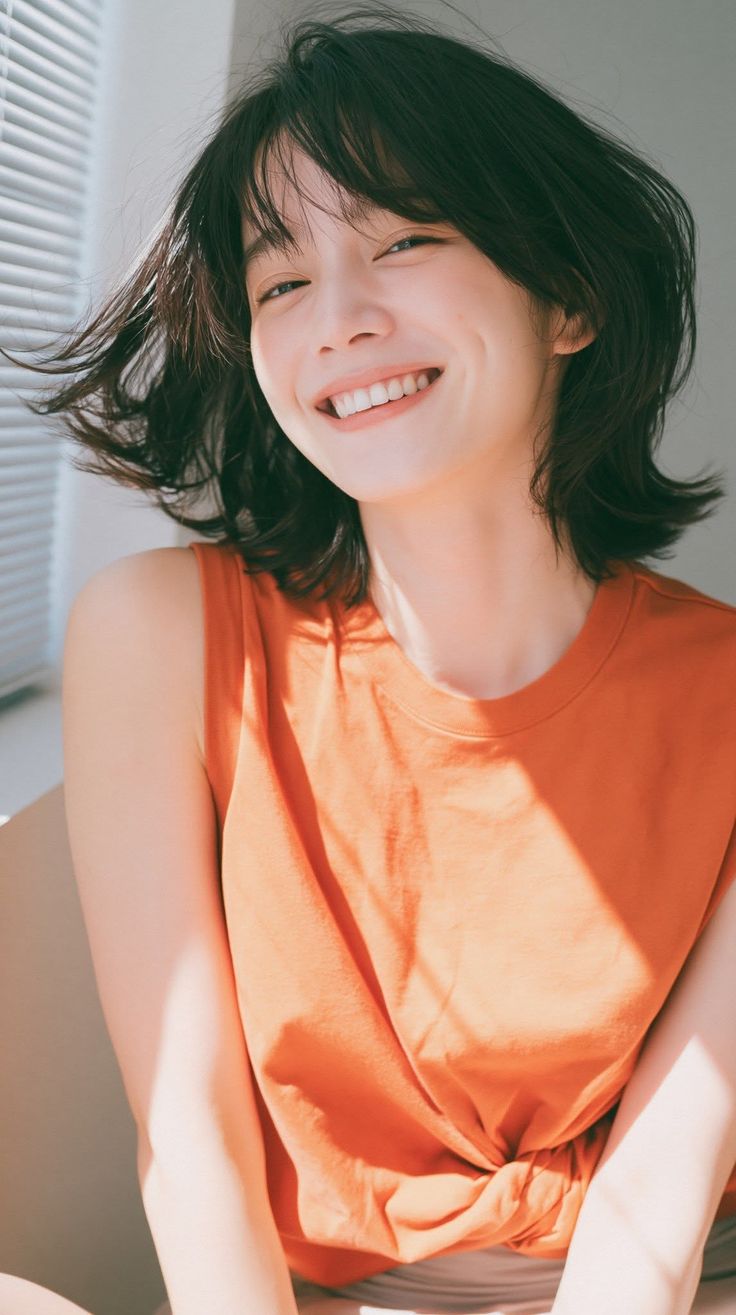 Woman with short hair and an orange top smiling in soft indoor lighting
