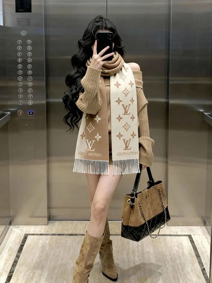 Woman in an off-shoulder sweater and scarf taking a mirror selfie in an elevator