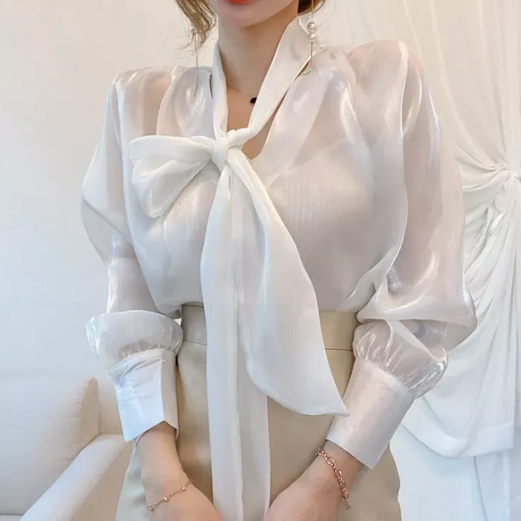 Woman in a sheer white blouse with a large bow collar and pearl earrings