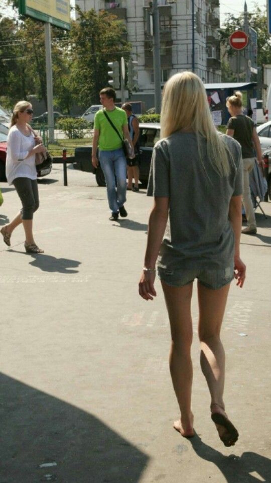 Blonde woman in denim shorts walking barefoot on a street with other people