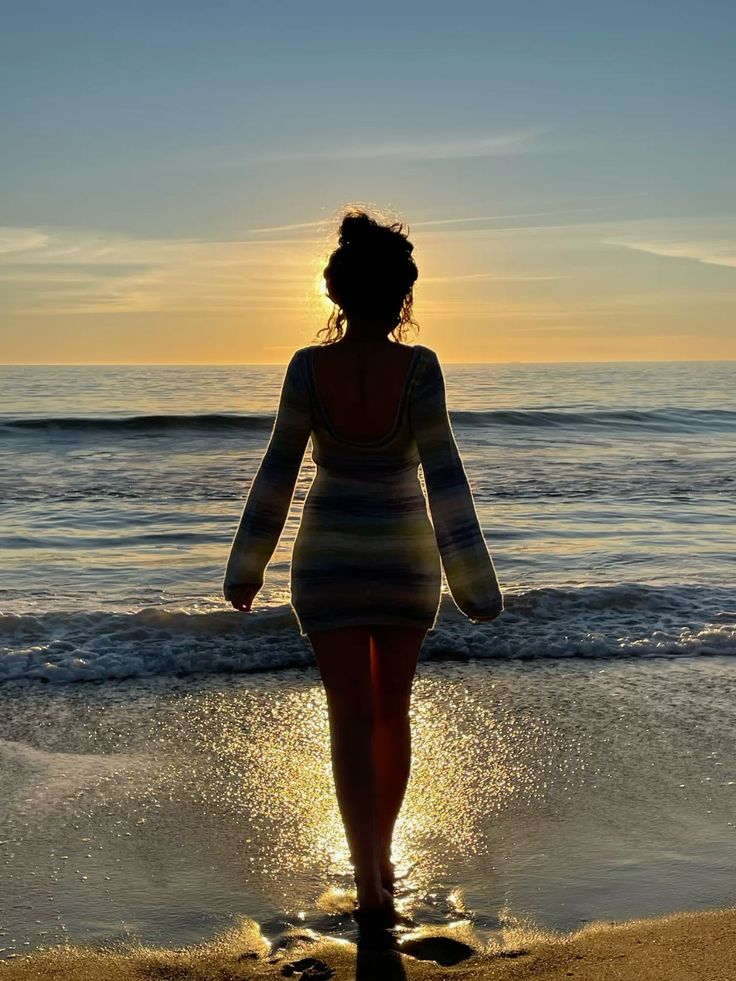 Woman in a long sleeve dress walking on a beach at sunset