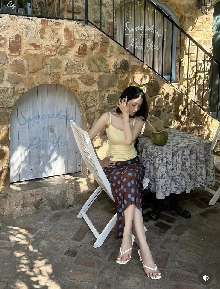Woman with long hair sitting outdoors at a cafe with a polka dot skirt