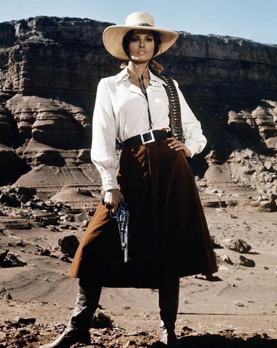 Woman in a cowgirl hat and western wear holding a revolver in a desert landscape