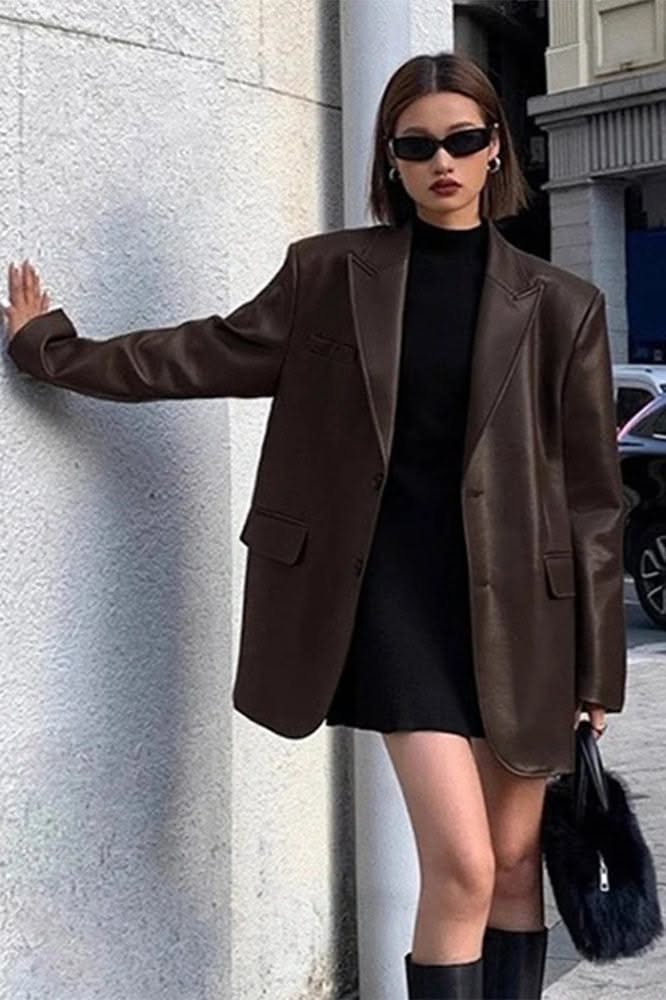 Woman in a brown blazer and black dress posing on a street