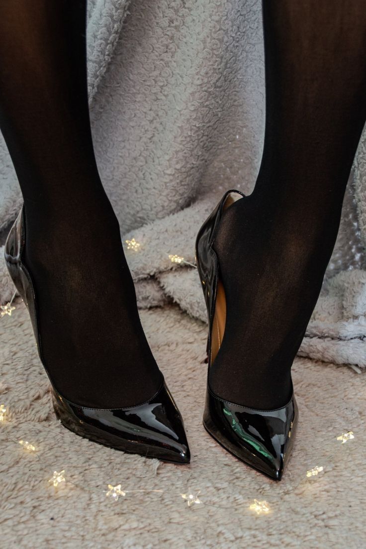 Legs in black tights and patent leather high heels on a textured surface