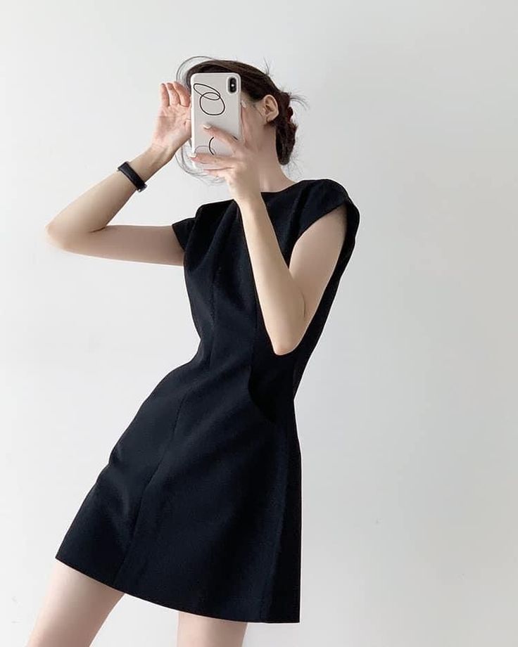 Woman in a black dress taking a mirror selfie indoors