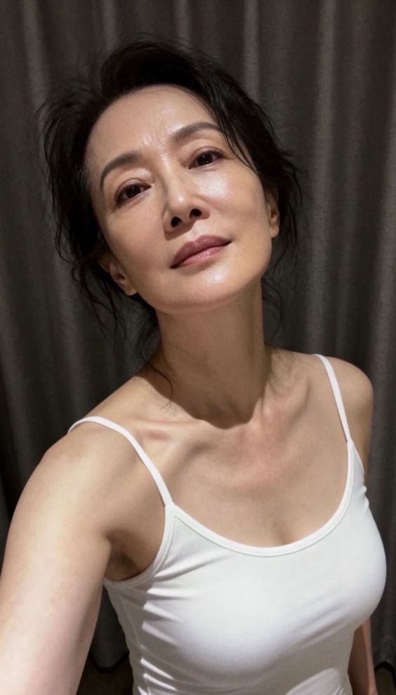 Woman with black hair wearing a white tank top indoors