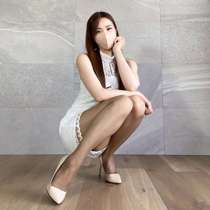 Woman in a white dress and face mask squatting indoors