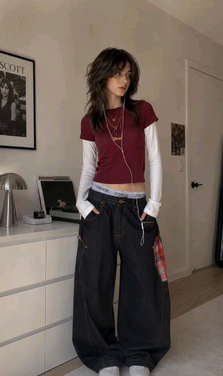 Woman with a shag haircut wearing a cropped top and baggy jeans indoors