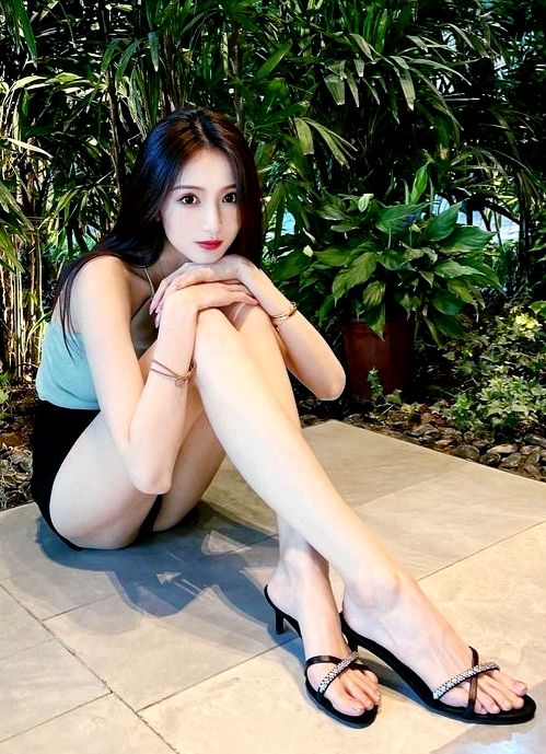 Woman with long dark hair sitting outdoors in black shorts and heeled sandals