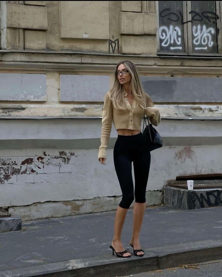 Woman with long hair and glasses wearing a cropped cardigan and capris on a street