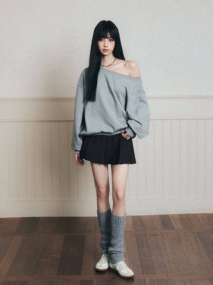 Woman with long black hair wearing an off-shoulder top and pleated skirt indoors